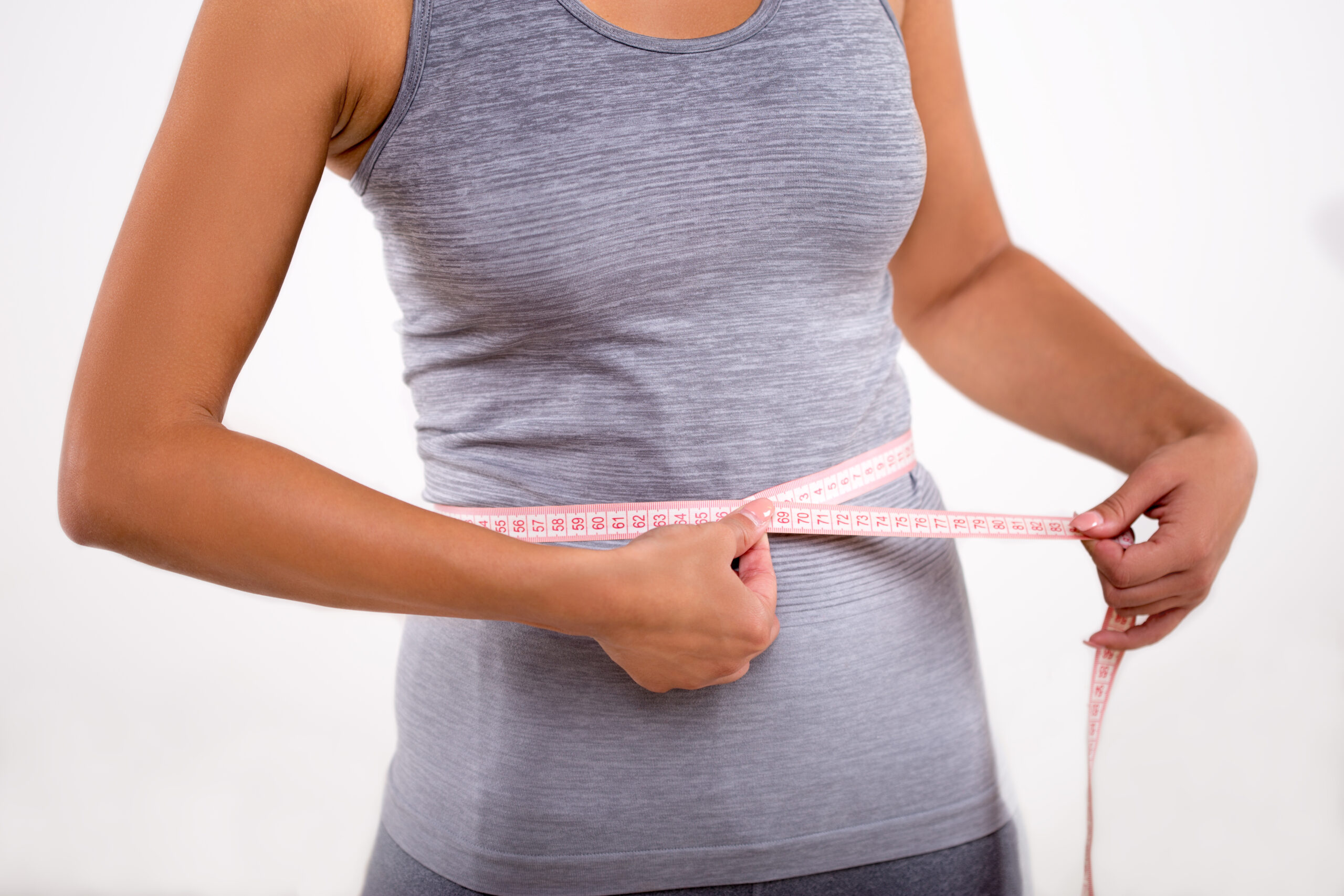 Happy fitness girl measuring her waist with tape measure